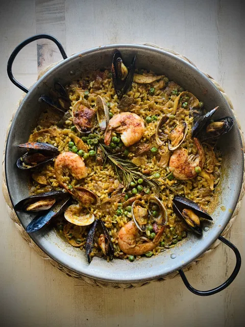 A seafood paella with shrimp, mussels, clams, rice, and peas in a wide handled pan.