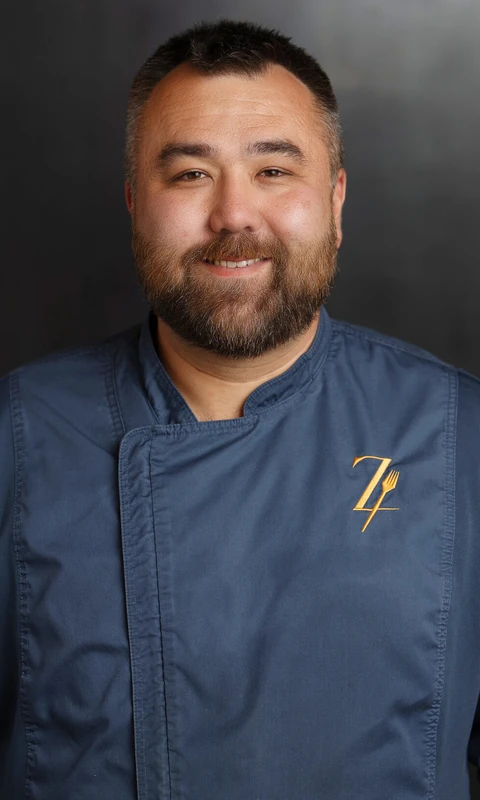 Shun Viger smiling in his blue chef coat in the exact portrait supplied by Archer.